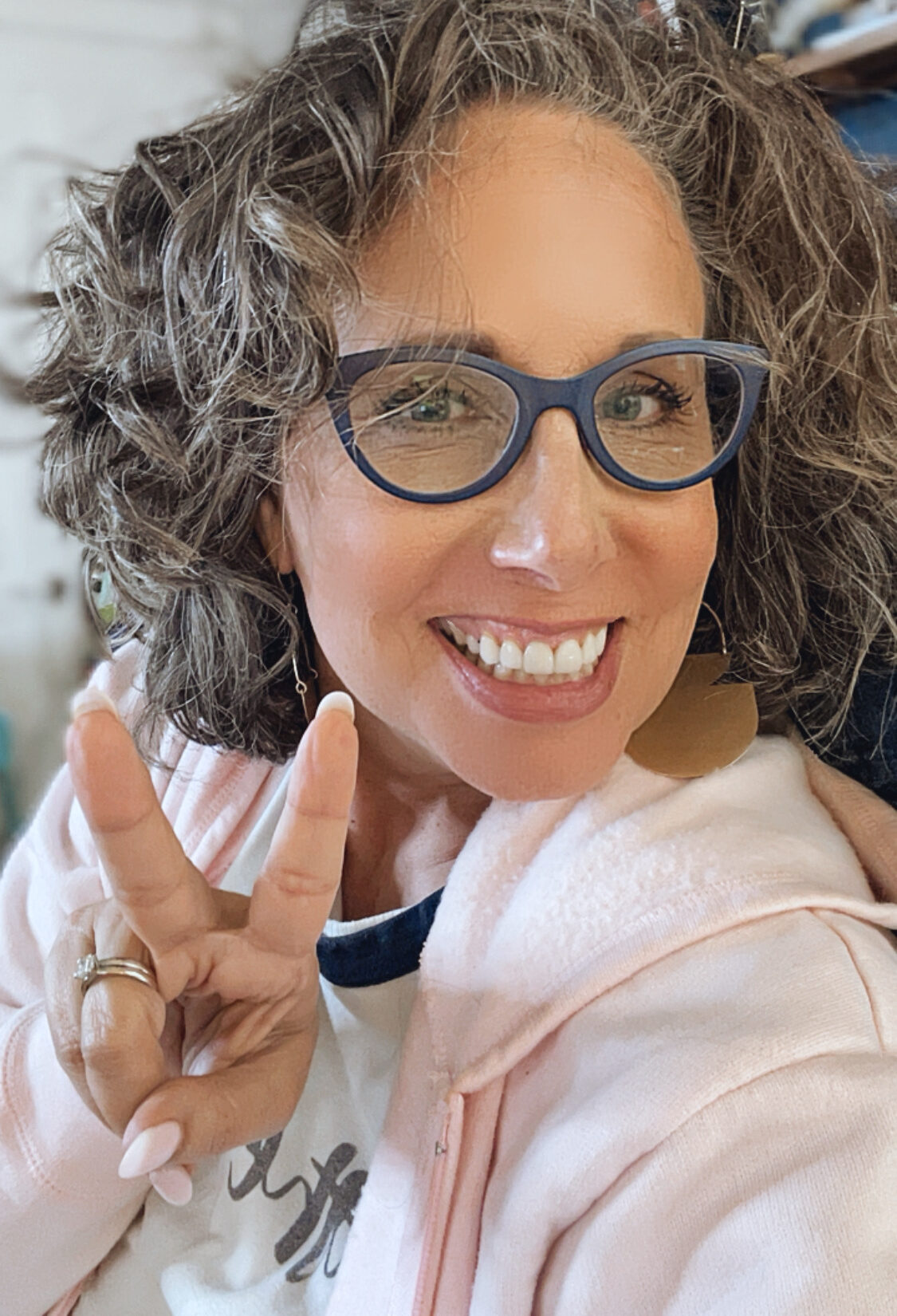 Smiling allison holding a peace sign and wearing a light pink hoodie