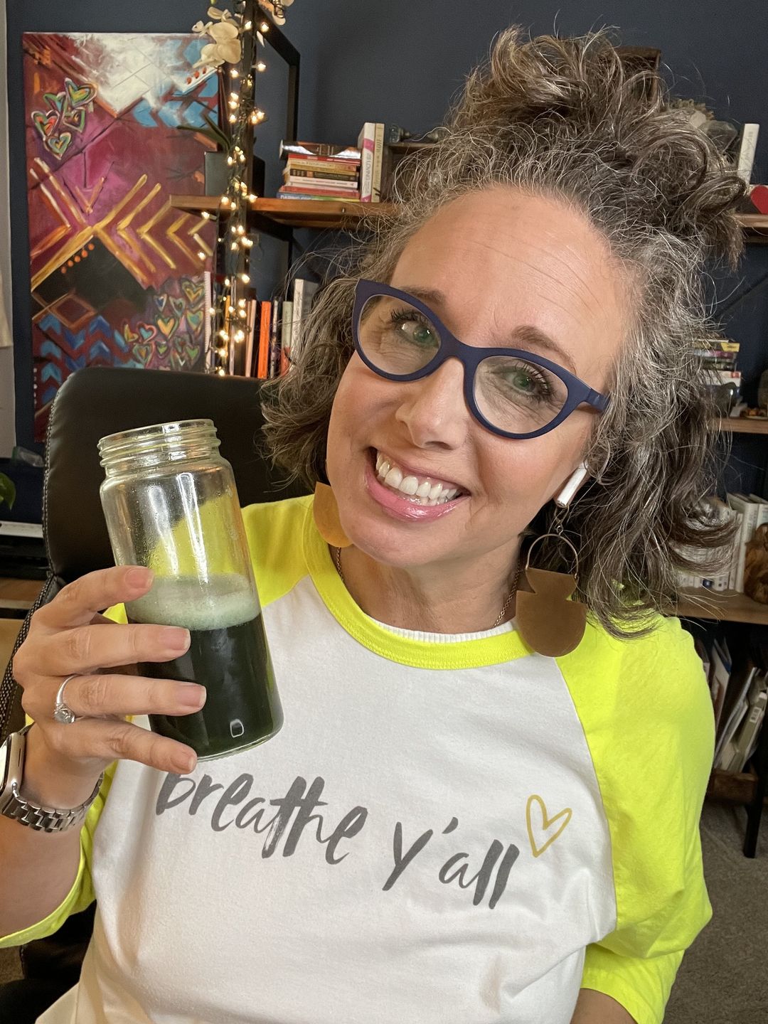 Allison in yellow and white tshirt holding a jar of green nutrient juice with a big smile on her face.