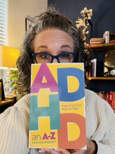 Allison peeking out from behind the book ADHD Figuring it OUt Step By Step; An A-Z by Leanne Maskell 
