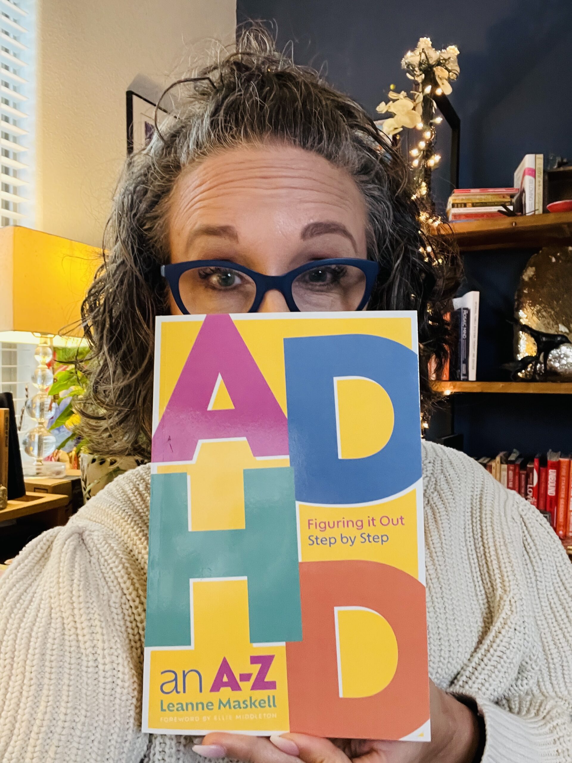 Allison peeking out from behind the book ADHD Figuring it OUt Step By Step; An A-Z by Leanne Maskell