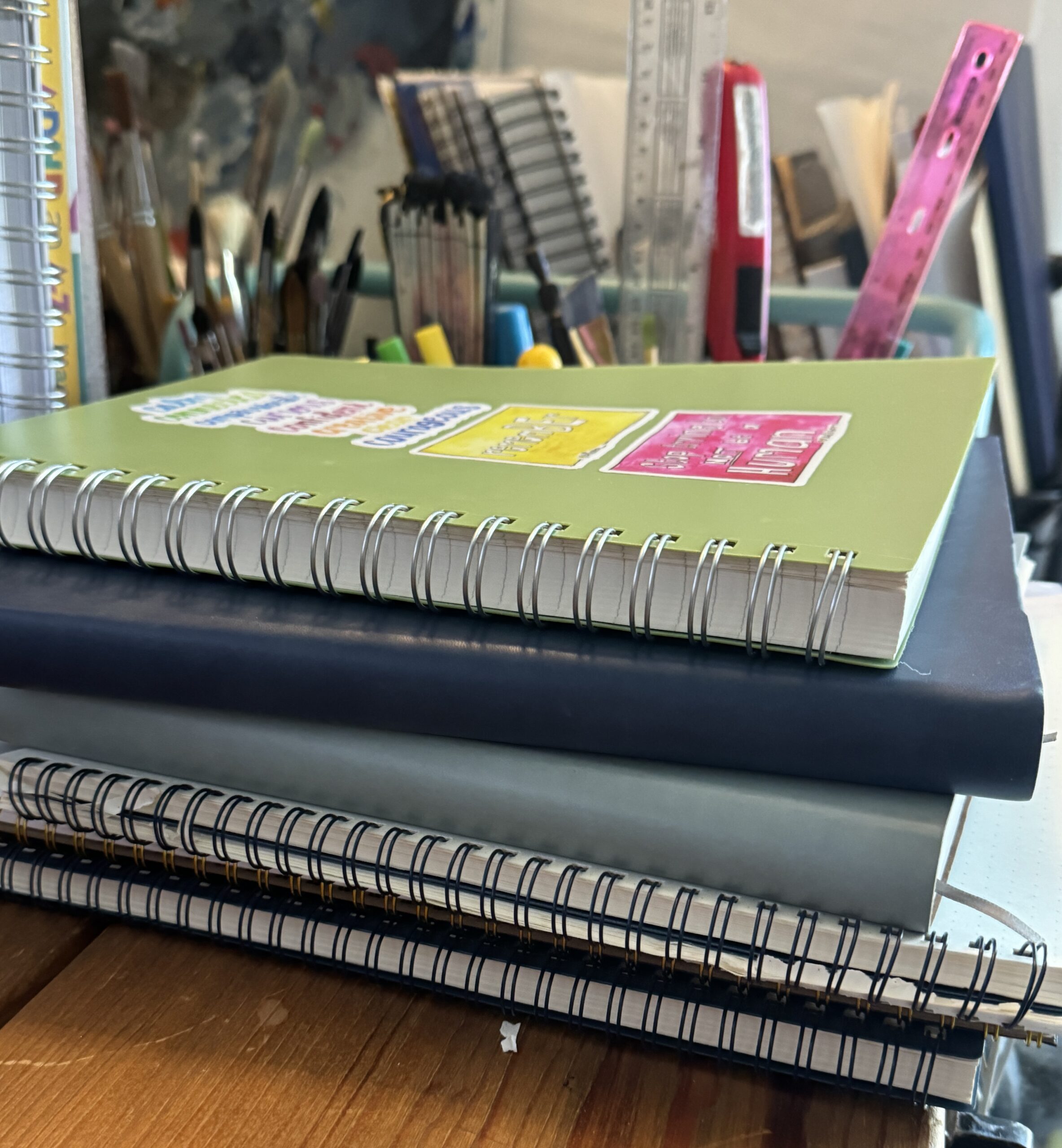 A stack of spiral and leather bound journals on allison's desk.
