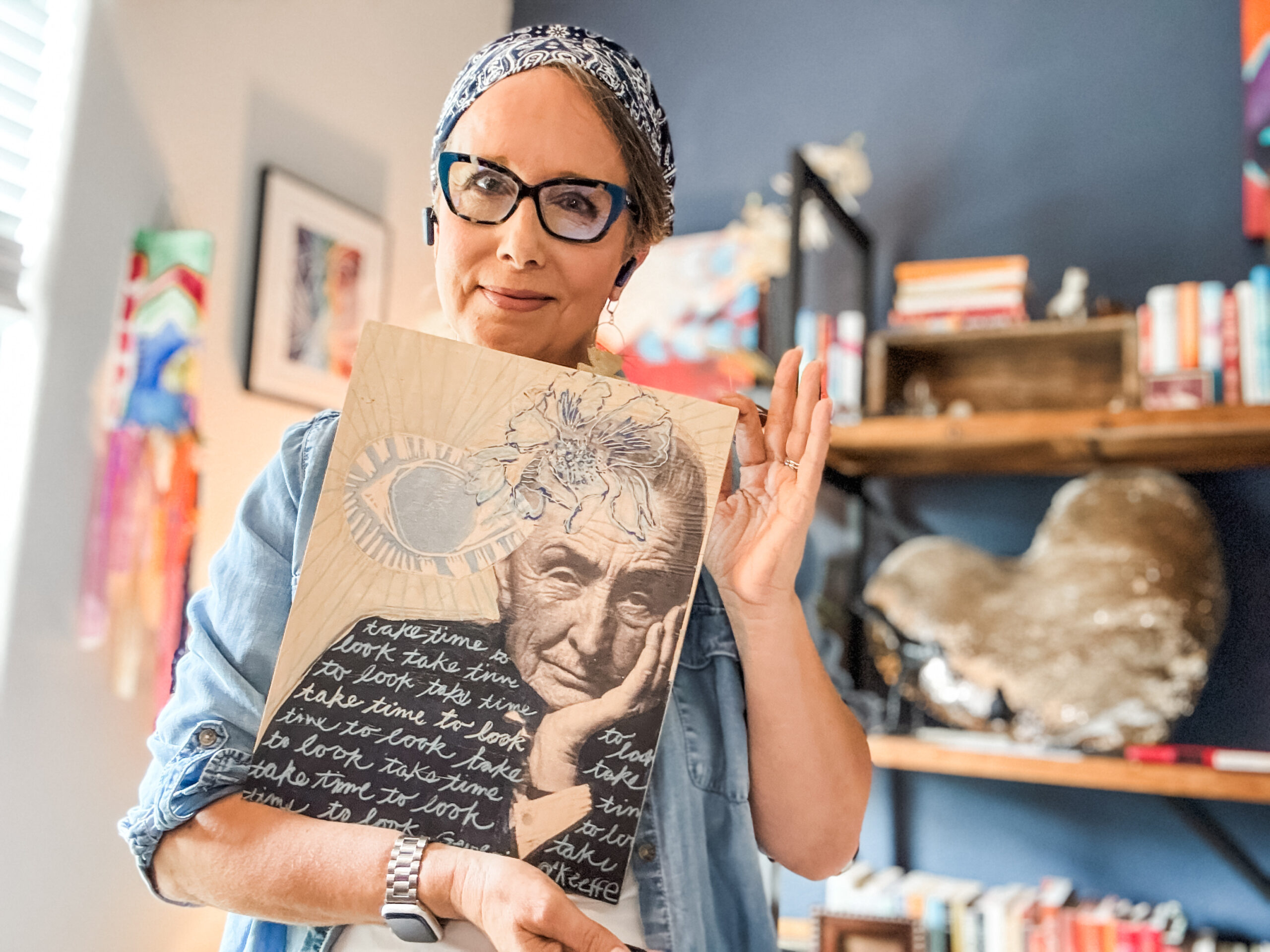 Allison holding a wood print by Sarah Bamford Seidlemann of with an image of Georgia O'Keeffe and the words ,"take time to look" painted multiple times.